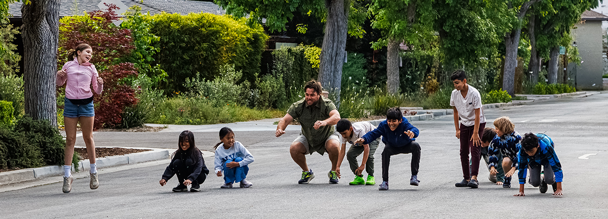 Teacher Craig duck-walks with the kids.