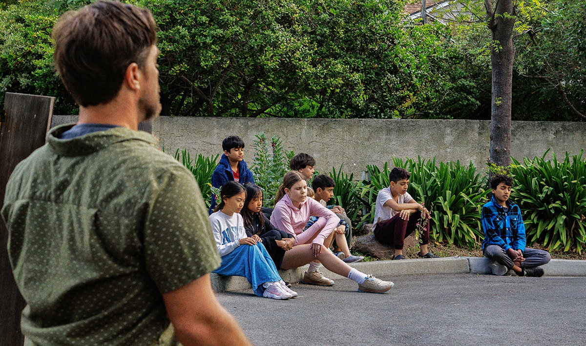 Kids meditate outdoors with teacher Craig Kellogg.