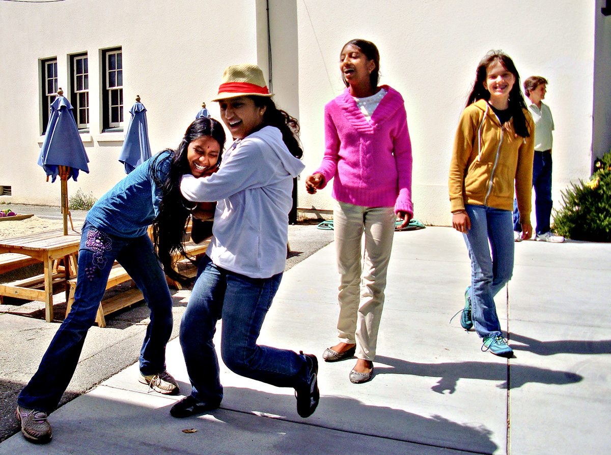Middle school girls laugh while trying to take possession of a basketball.