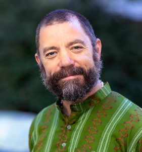Martial arts instructor and PhysEd teacher David James, portrait photo taken outdoors wearing green Gandhi collar shirt and smiling.