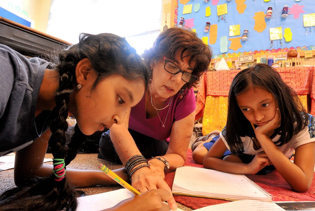 Ruth silver on floor helping two girls with math in third grade.