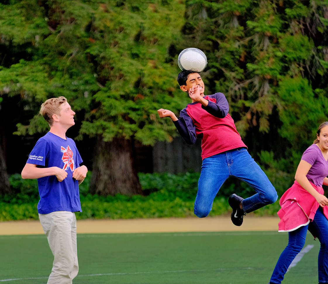 Middle school boys play soccer - a talented boy leaps high to advance the ball with a header.